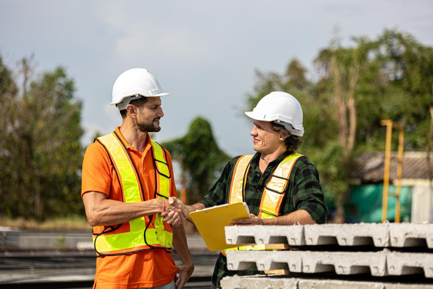 Two contractors in hard hats shaking hands on a job site