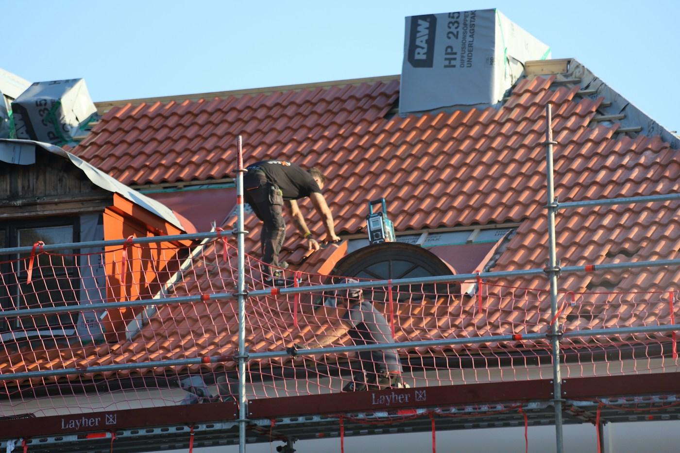 A roofer working on a tiled roof behind scaffolding